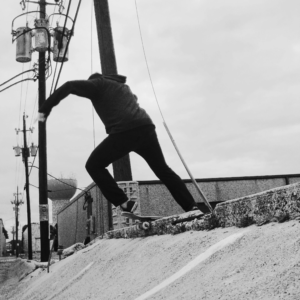 man doing a rock n roll on a skateboard on a banked wall with a curb at the top