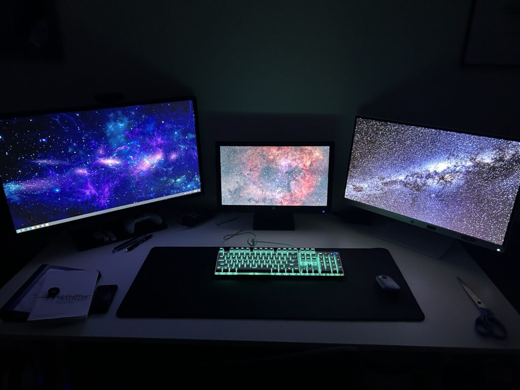 3 computer monitors on a desk with a blue-lit keyboard